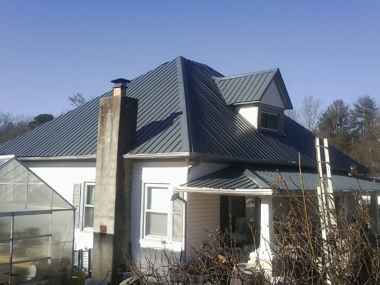 Dark blue standing seam metal roof on a white farmhouse with dormer — Slate & Tile Roof Repair by Roofing Brothers in Eastview