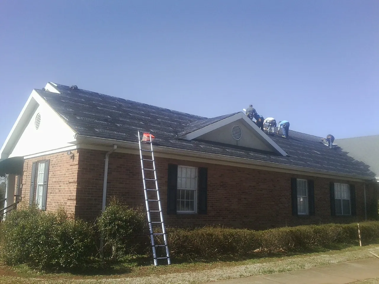 Crew tearing shingles off a brick ranch roof with a ladder set — Metal Roof Repair work by our crew in Eastview
