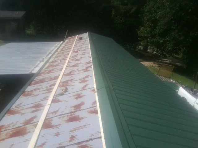 Old rusted panels beside newly installed green metal roofing — Wind Damage Roof Repair by Roofing Brothers in Eastview