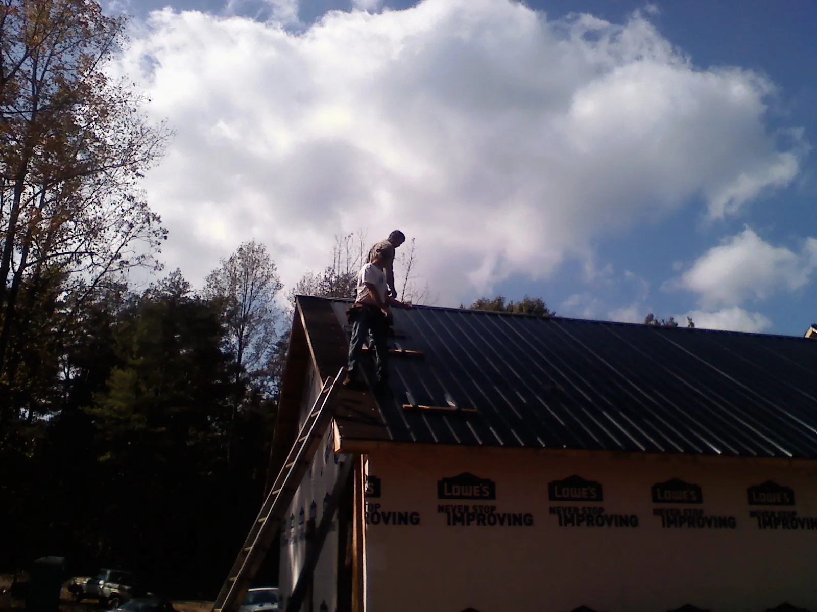 Roofer fastening dark metal panels high against a cloudy sky, from a Roof Inspection job in Eastview